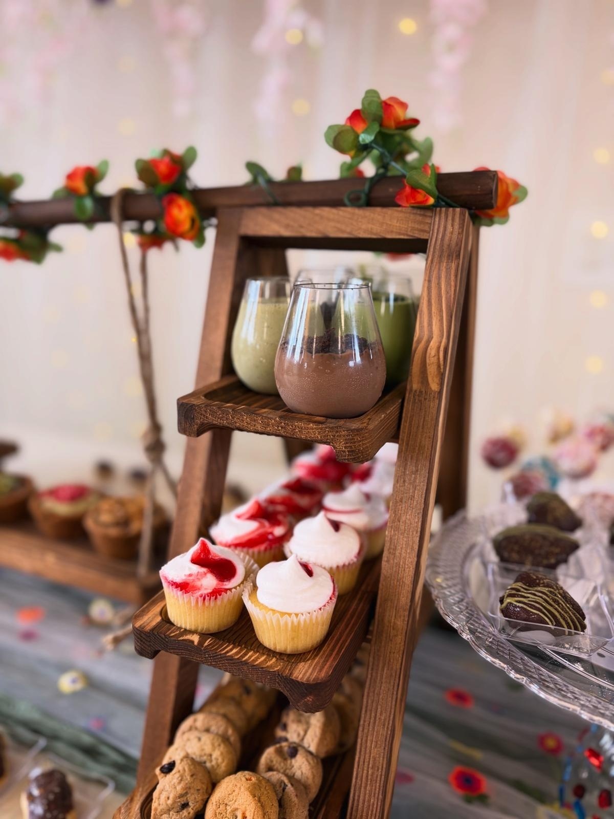 Tiered wooden ladder stand with pistachio and chocolate dessert shooters, strawberry cupcakes and cookies