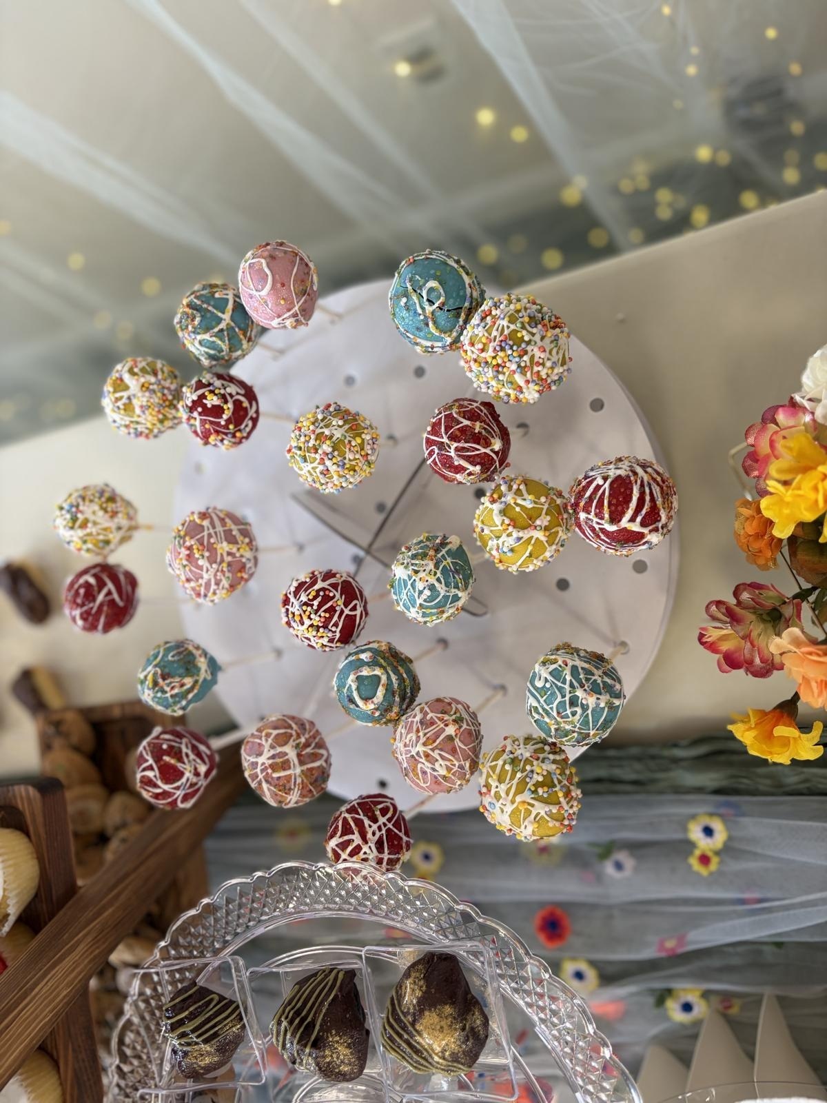 Overhead view of colorful sprinkle-coated cake pops arranged on a white round display stand